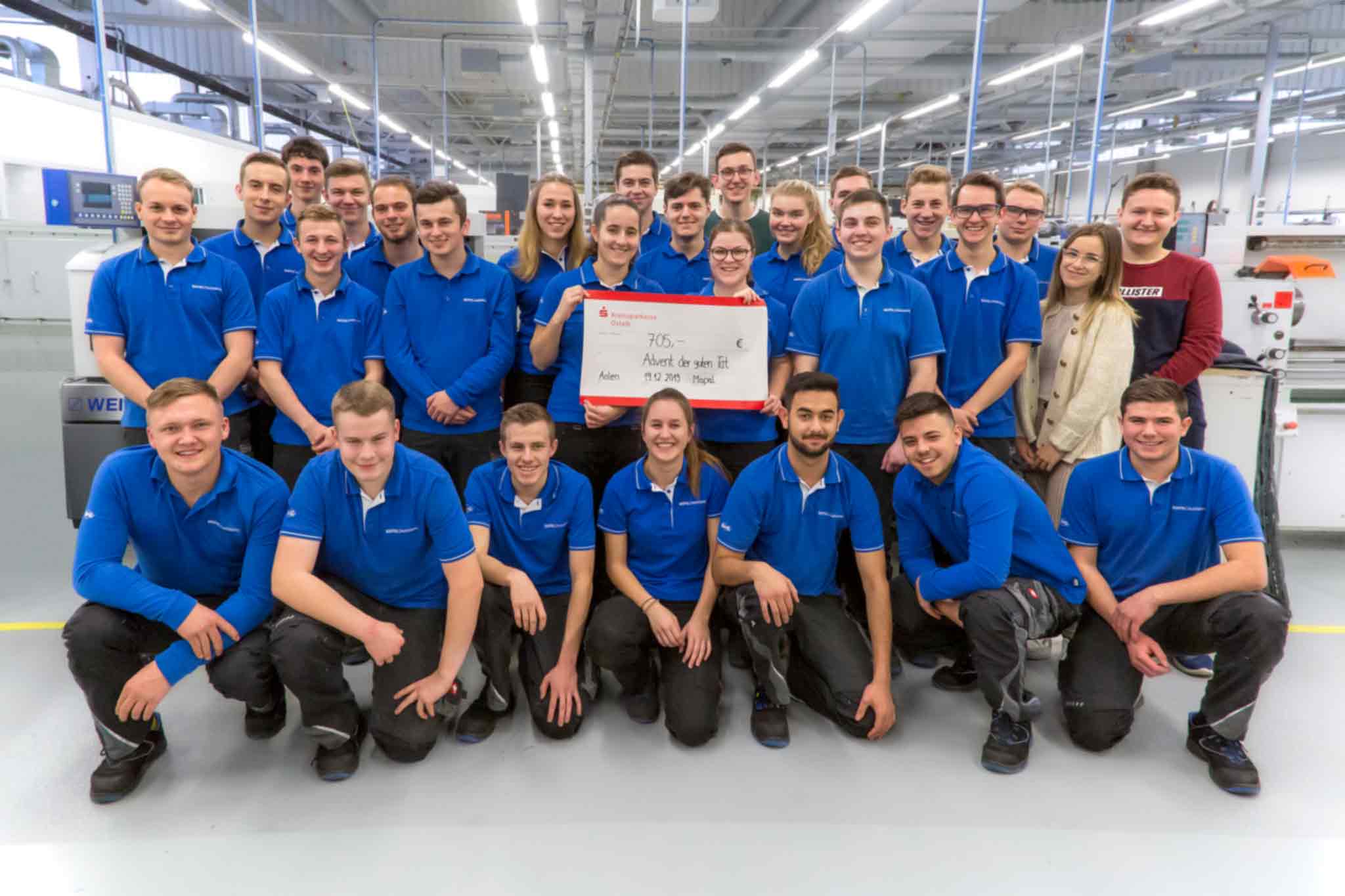 28 apprentices from MAPAL present a large donation cheque. They are at the MAPAL Training Centre.